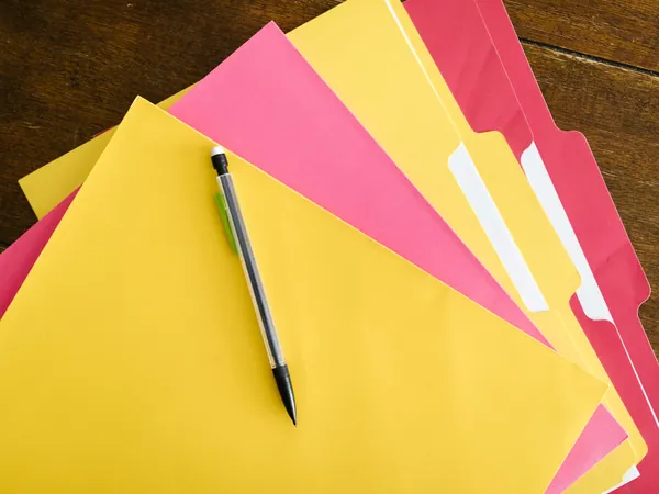 Gekleurde dossiermappen en een potlood op een houten tafel